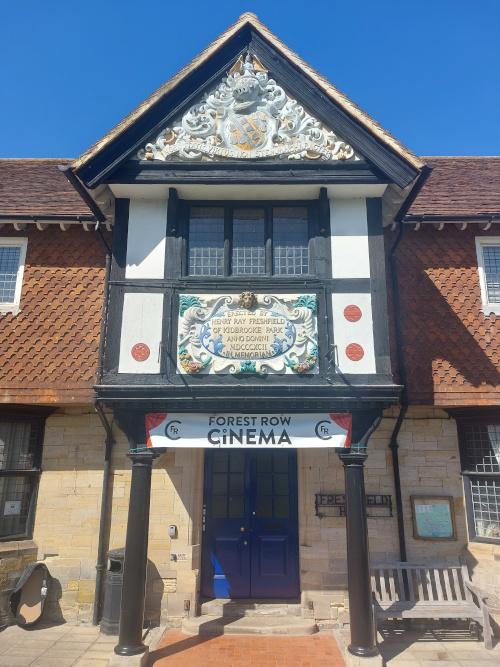 The decorated gable of Forest Row Village Hall with a memorial to Henry Ray Freshfield of Kidbrooke Park, dated 1892. There is also a banner above the door reading Forest Row Cinema